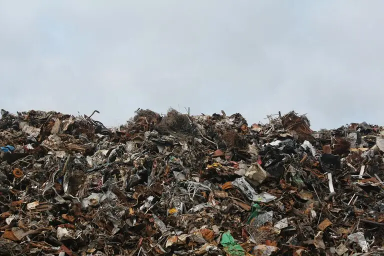 A large pile of scrap metal and waste at a landfill against a cloudy sky.