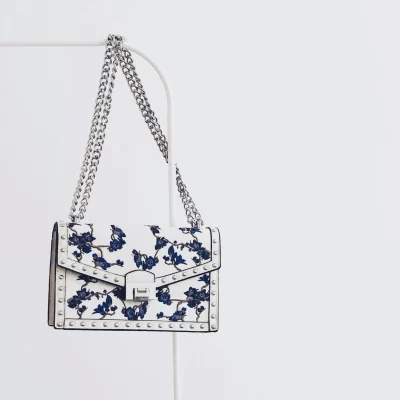 Elegant white handbag with blue floral design and silver chain, perfect for fashion enthusiasts.